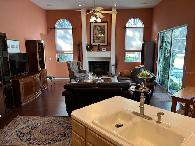 living room with a tiled fireplace, sink, a towering ceiling, and dark wood-type flooring