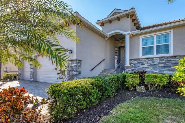 view of front of property featuring stucco siding, stone siding, an attached garage, and decorative driveway