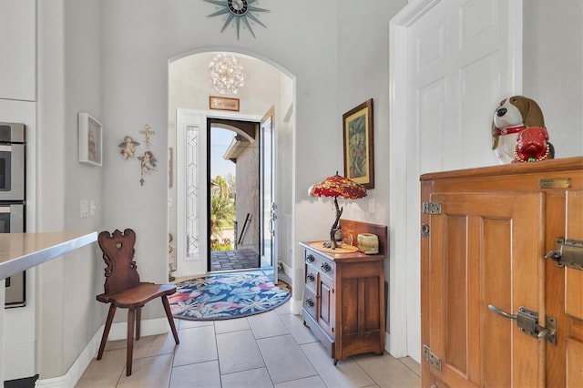 foyer entrance with light tile patterned floors, a notable chandelier, arched walkways, and baseboards