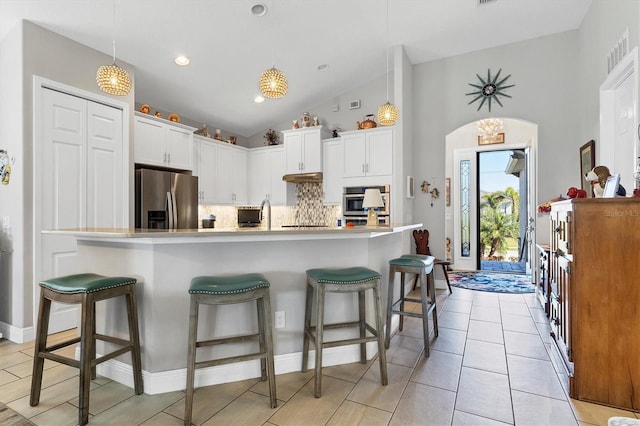 kitchen featuring a kitchen breakfast bar, tasteful backsplash, white cabinetry, stainless steel fridge, and arched walkways