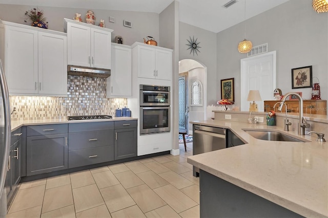 kitchen featuring gray cabinets, a sink, under cabinet range hood, arched walkways, and appliances with stainless steel finishes