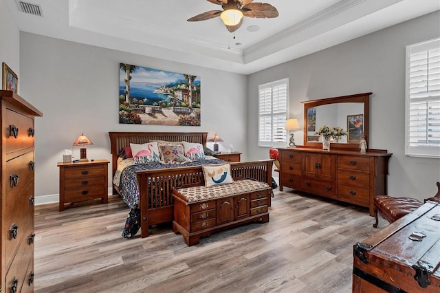 bedroom featuring visible vents, light wood-style flooring, crown molding, and a tray ceiling