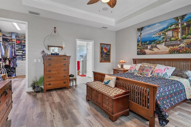 bedroom featuring visible vents, light wood finished floors, crown molding, a walk in closet, and a raised ceiling