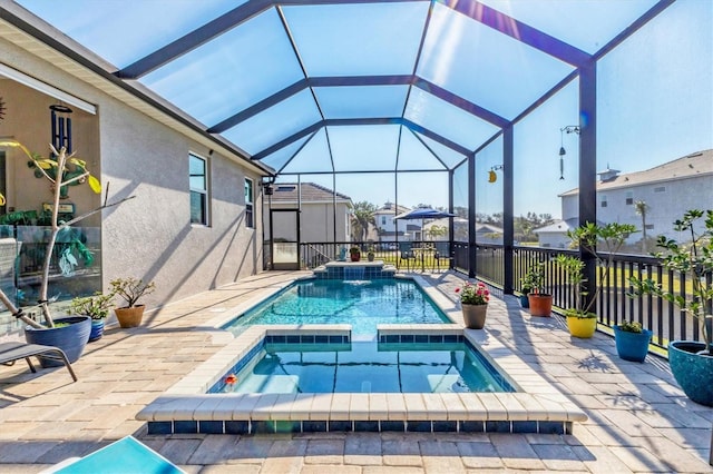 view of pool featuring glass enclosure, a pool with connected hot tub, and a patio