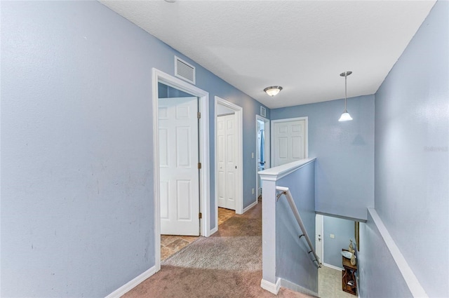 hall with visible vents, carpet flooring, a textured ceiling, an upstairs landing, and baseboards