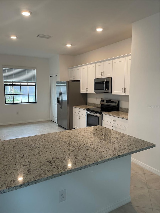 kitchen featuring light stone counters, light tile patterned floors, appliances with stainless steel finishes, kitchen peninsula, and white cabinets