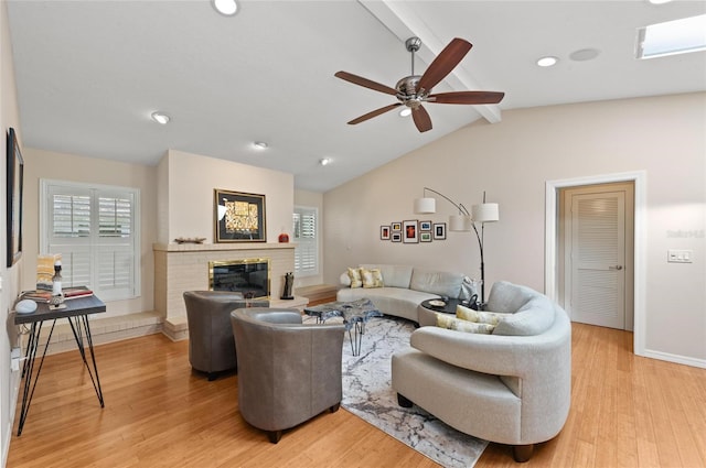 living room featuring ceiling fan, a brick fireplace, light hardwood / wood-style flooring, and vaulted ceiling with beams