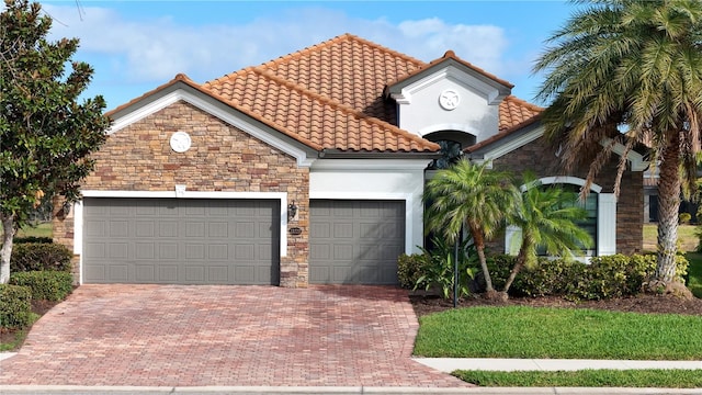 mediterranean / spanish home featuring an attached garage, a tile roof, stone siding, decorative driveway, and stucco siding