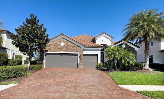 mediterranean / spanish house featuring a garage, stone siding, a tiled roof, decorative driveway, and stucco siding