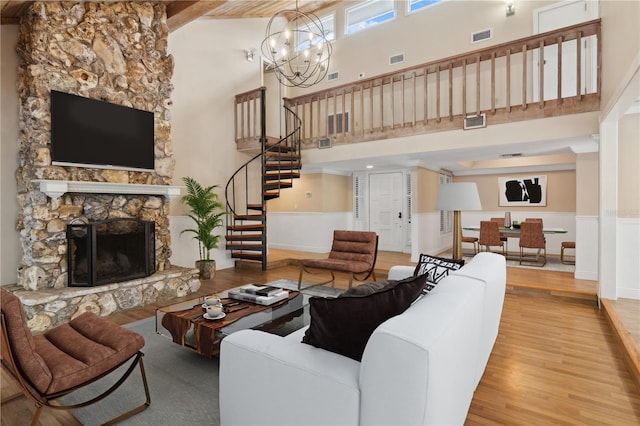 living room featuring a notable chandelier, a stone fireplace, a towering ceiling, and hardwood / wood-style floors