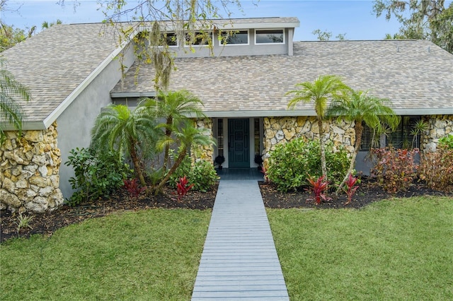 view of front facade featuring stone siding, a shingled roof, a front yard, and stucco siding