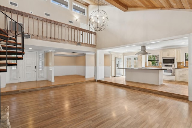 unfurnished living room with a high ceiling, light wood finished floors, stairway, a chandelier, and wainscoting