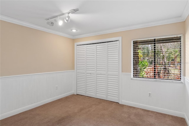 unfurnished bedroom with wainscoting, crown molding, carpet floors, a closet, and track lighting