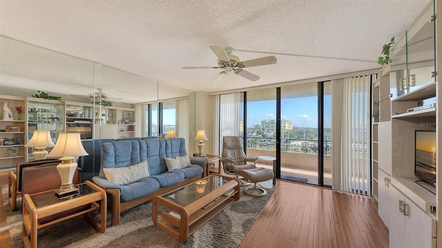 living room featuring wood-type flooring, a textured ceiling, ceiling fan, and a wall of windows