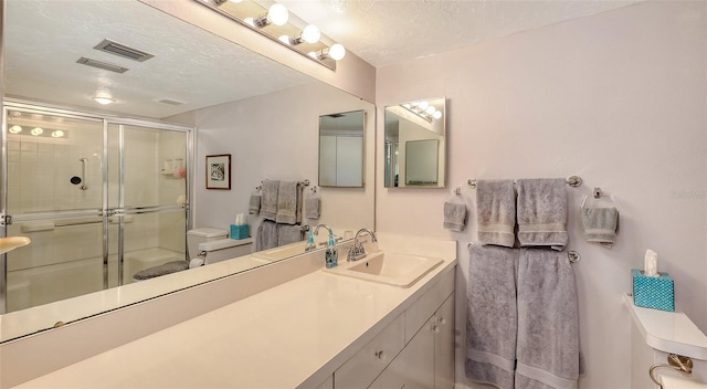 bathroom featuring a shower with door, vanity, a textured ceiling, and toilet