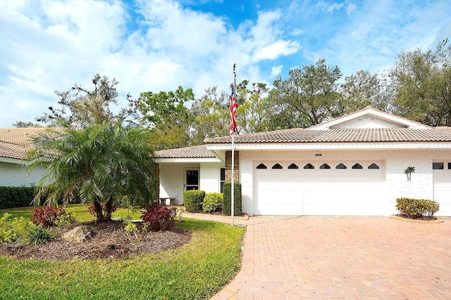 view of front of home featuring stucco siding, an attached garage, a tile roof, and decorative driveway