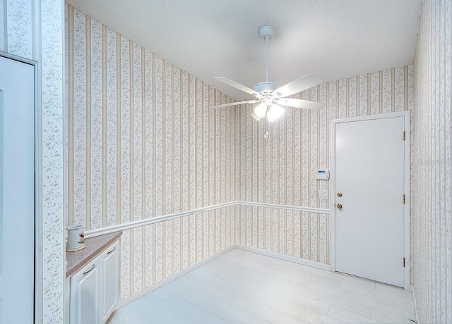 unfurnished room with wood finished floors, a textured ceiling, ceiling fan, and wallpapered walls