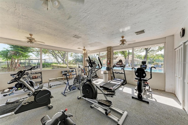 gym with ceiling fan, visible vents, and a textured ceiling