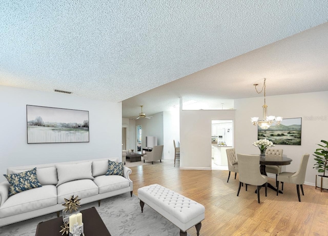 living area with visible vents, baseboards, a textured ceiling, and light wood finished floors