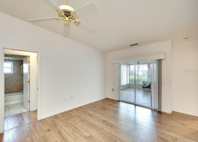 empty room with visible vents, light wood-type flooring, vaulted ceiling, a textured ceiling, and a ceiling fan