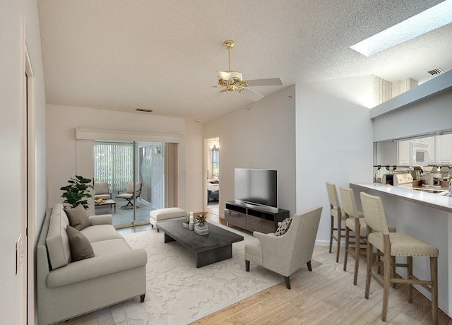 living room featuring visible vents, vaulted ceiling with skylight, light wood-style floors, and a textured ceiling