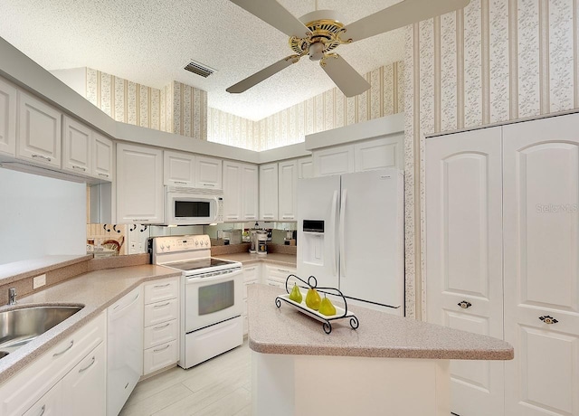 kitchen featuring white appliances, visible vents, wallpapered walls, a textured ceiling, and a center island