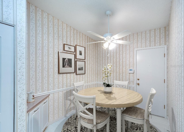 dining space with wallpapered walls, a ceiling fan, baseboards, and a textured ceiling