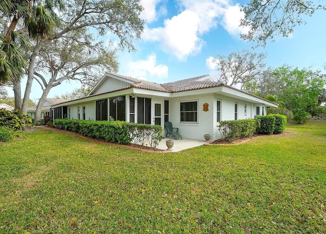 rear view of property with a lawn, a tile roof, a patio, and a sunroom