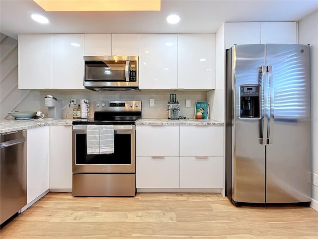 kitchen featuring appliances with stainless steel finishes, backsplash, white cabinets, light stone counters, and light hardwood / wood-style floors