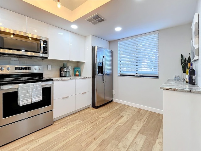 kitchen with light hardwood / wood-style flooring, white cabinetry, backsplash, stainless steel appliances, and light stone countertops