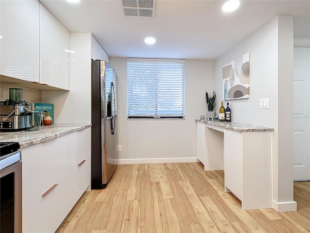 kitchen with white cabinetry, stainless steel appliances, light stone counters, and light wood-type flooring