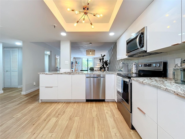 kitchen with white cabinetry, hanging light fixtures, kitchen peninsula, a raised ceiling, and stainless steel appliances