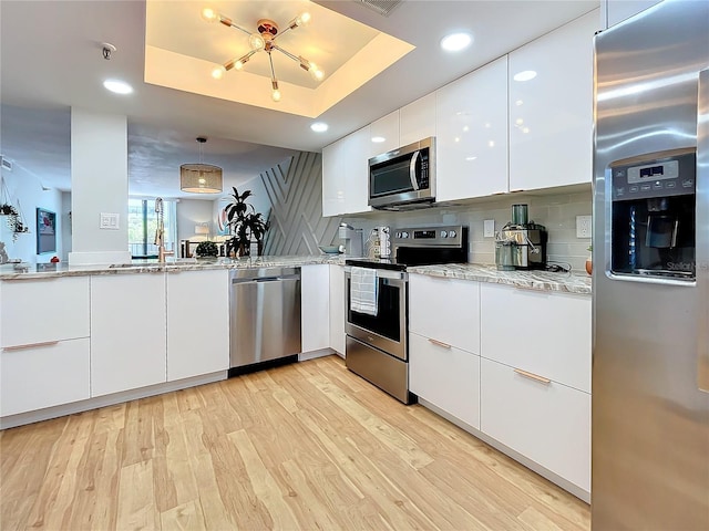 kitchen featuring appliances with stainless steel finishes, pendant lighting, sink, white cabinets, and a tray ceiling