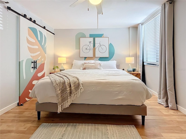 bedroom with ceiling fan, wood-type flooring, and a barn door