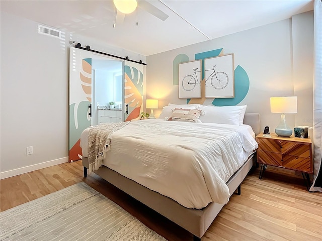 bedroom featuring ceiling fan, a barn door, and light wood-type flooring