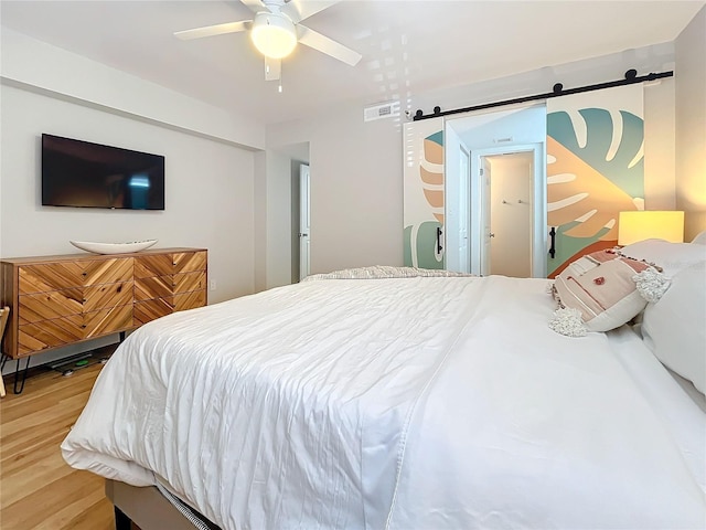 bedroom featuring ceiling fan, wood-type flooring, and a barn door