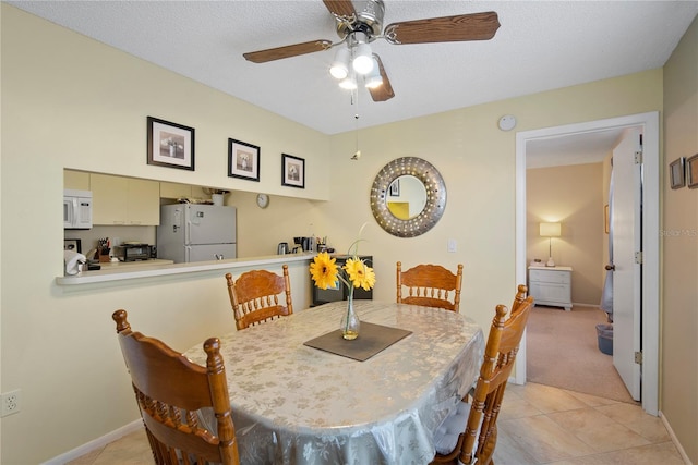 tiled dining space with a textured ceiling and ceiling fan