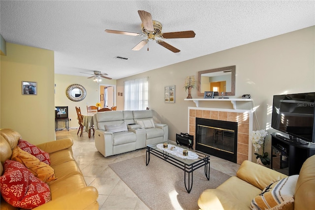 living room with a tile fireplace, light tile patterned floors, ceiling fan, and a textured ceiling