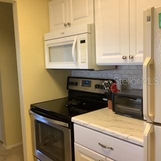 kitchen featuring tasteful backsplash, light stone countertops, white cabinets, and white appliances