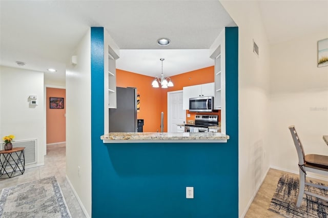 kitchen featuring pendant lighting, appliances with stainless steel finishes, white cabinetry, light stone counters, and a chandelier