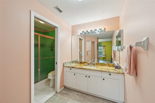 bathroom featuring a shower with door, vanity, a textured ceiling, tile patterned floors, and toilet