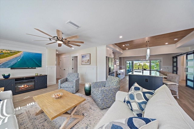 living room featuring ceiling fan, a barn door, and light hardwood / wood-style floors