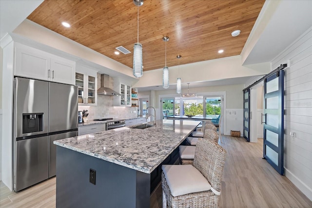 kitchen featuring wall chimney range hood, sink, appliances with stainless steel finishes, a spacious island, and a barn door