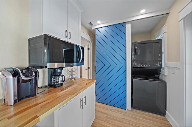 kitchen featuring stacked washer and dryer, wooden counters, white cabinets, and light hardwood / wood-style flooring