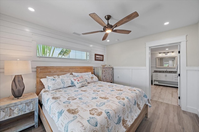 bedroom featuring ceiling fan, ensuite bath, and light wood-type flooring