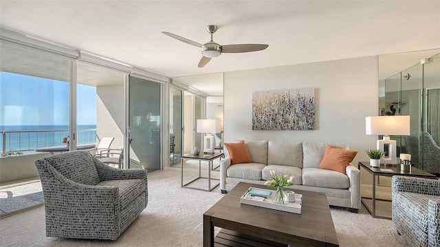 living room featuring light carpet, floor to ceiling windows, ceiling fan, and a water view