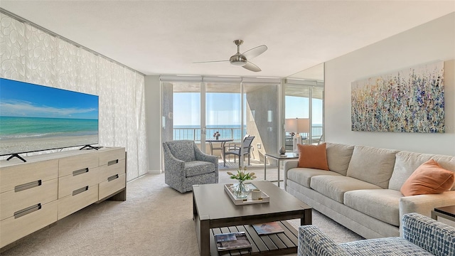 living room with a water view, a wall of windows, ceiling fan, and light colored carpet