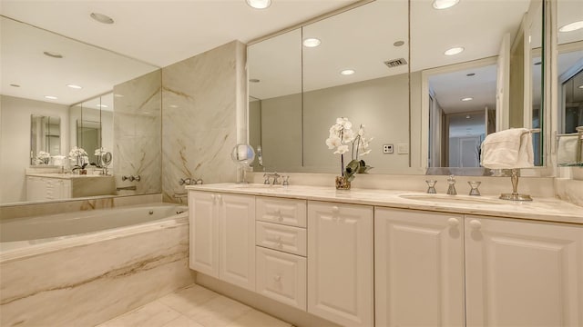 bathroom with tiled tub, vanity, and tile patterned flooring