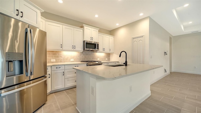 kitchen with sink, white cabinetry, stainless steel appliances, light stone countertops, and an island with sink