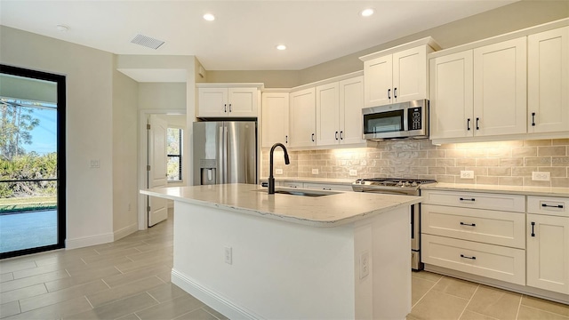 kitchen with appliances with stainless steel finishes, white cabinetry, sink, a kitchen island with sink, and light stone counters